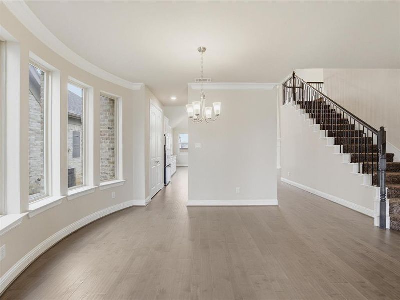 Spacious interior featuring wood-finish flooring, a contemporary chandelier, a curved wall with multiple windows, a staircase with dark wood newel posts and iron balusters, and crown molding