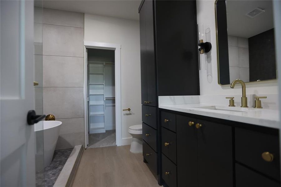 Full bath featuring a spacious closet, vanity, a freestanding bath, and light wood-style floors