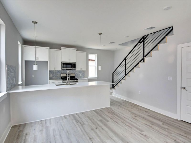 Kitchen with white cabinetry, a peninsula, hanging light fixtures, stainless steel appliances, and light wood-style flooring