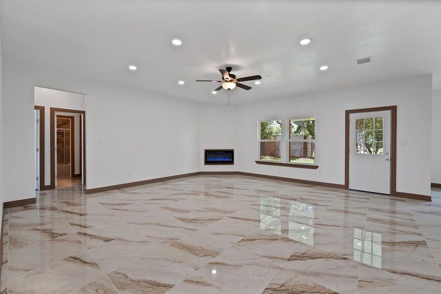 Unfurnished living room with light marble finish floors, recessed lighting, a ceiling fan, and a glass covered fireplace