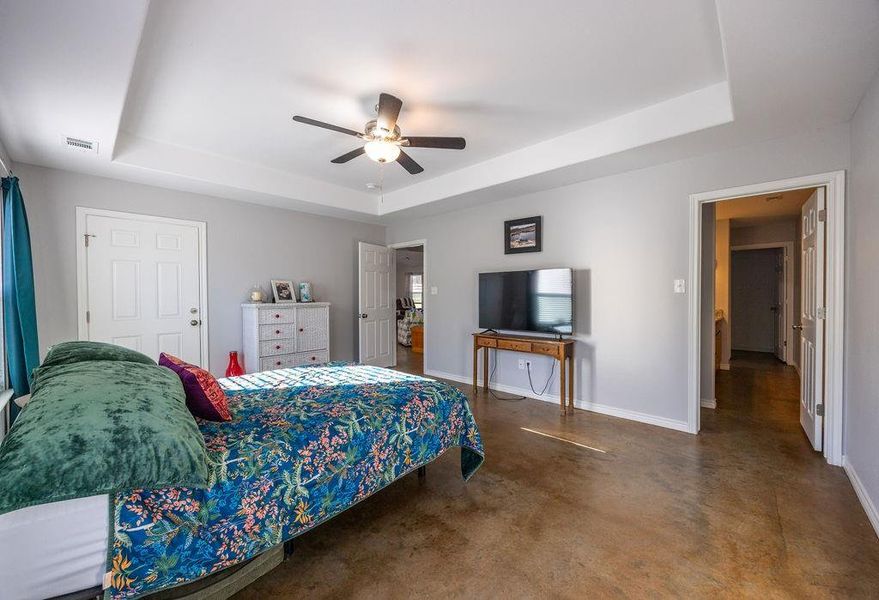 Bedroom with a tray ceiling, finished concrete flooring, and ceiling fan