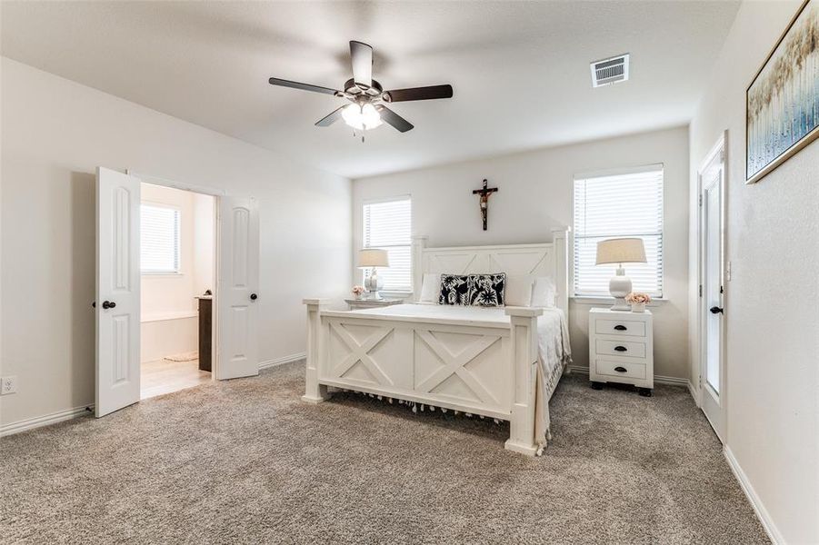 Bedroom with ensuite bathroom, ceiling fan, and light colored carpet