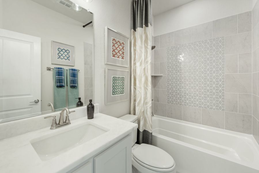 Full bathroom with white vanity, tub-shower combo with gray tile surround, and decorative wall art