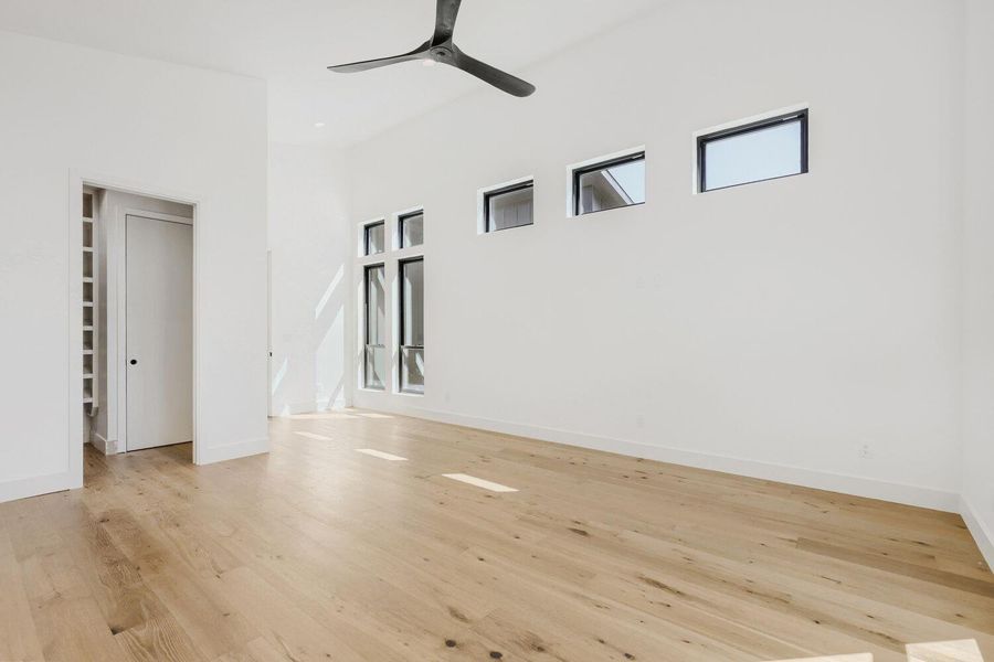 Empty room with light wood-type flooring, a high ceiling, and a ceiling fan Empty room with light wood-type flooring, a high ceiling, and a ceiling fan