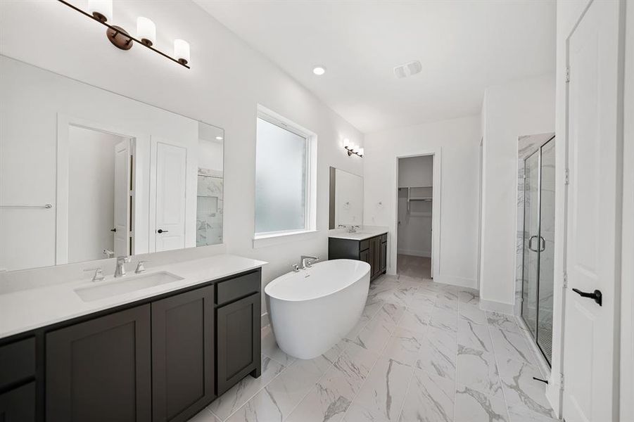 Full bathroom featuring a stall shower, a spacious closet, two vanities, a soaking tub, and light marble finish floors Full bathroom featuring a stall shower, a spacious closet, two vanities, a soaking tub, and light marble finish floors