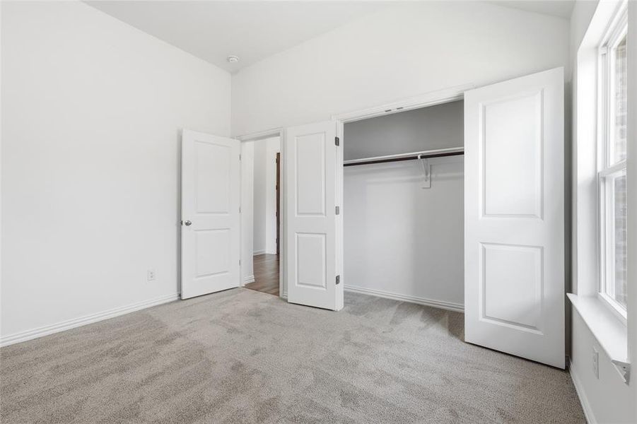 Carpeted room featuring a double-door closet with shelving and hanging rod, a single window, and a vaulted ceiling