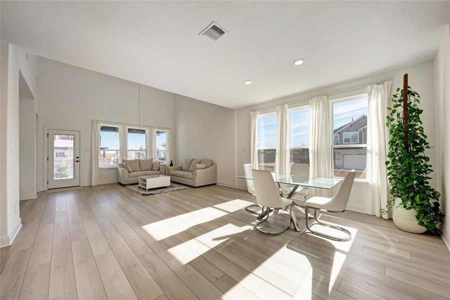 Expansive living and dining areas featuring high vaulted ceilings, wood-finish flooring, recessed lighting, and multiple large windows with white curtains