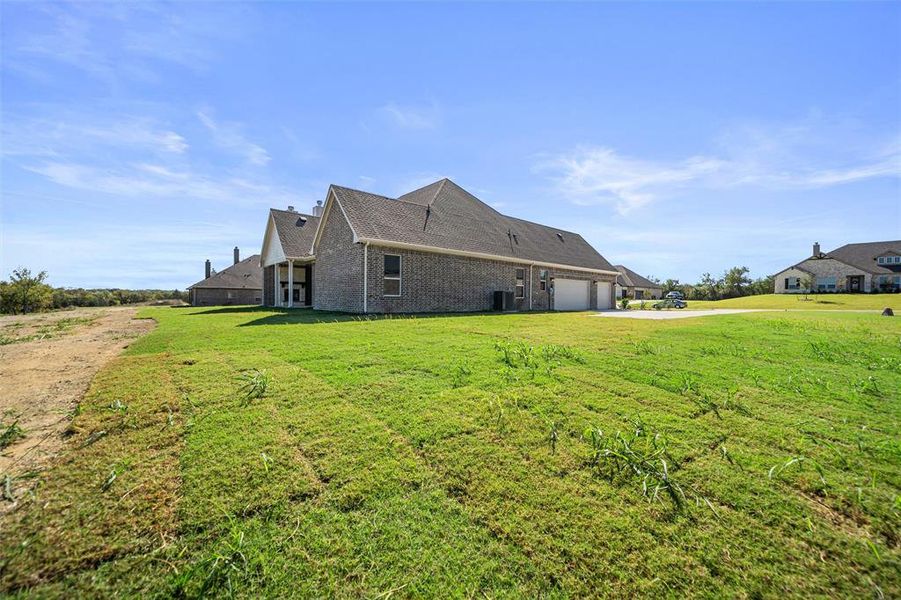 Rear view of house with brick siding, a lawn, an attached garage, roof with shingles, and driveway Rear view of house with brick siding, a lawn, an attached garage, roof with shingles, and driveway