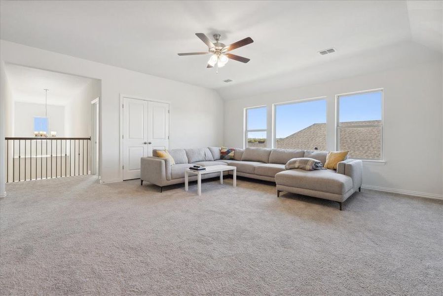 Living room with ceiling fan with notable chandelier, light colored carpet, and lofted ceiling