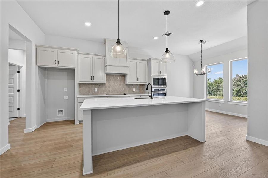 Open-concept kitchen featuring a large central island with a solid surface countertop, white shaker cabinetry, a geometric tile backsplash, and wood-finish flooring