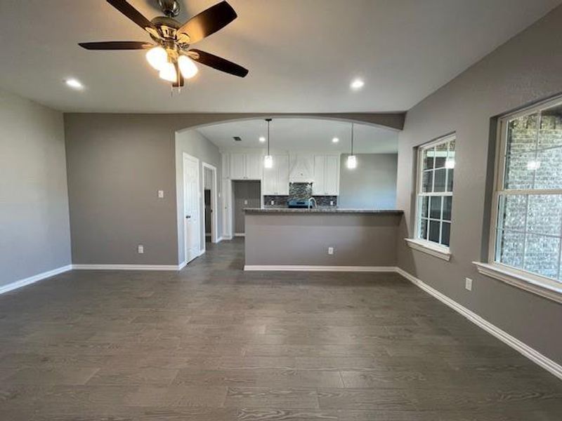Facing the kitchen with arched entry, wood-style floors, recessed lighting, white cabinetry, and baseboards Facing the kitchen with arched entry, wood-style floors, recessed lighting, white cabinetry, and baseboards