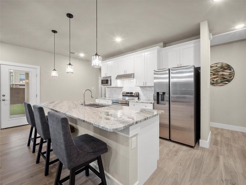 Kitchen featuring appliances with stainless steel finishes, a kitchen breakfast bar, backsplash, light stone counters, and white cabinetry Kitchen featuring appliances with stainless steel finishes, a kitchen breakfast bar, backsplash, light stone counters, and white cabinetry