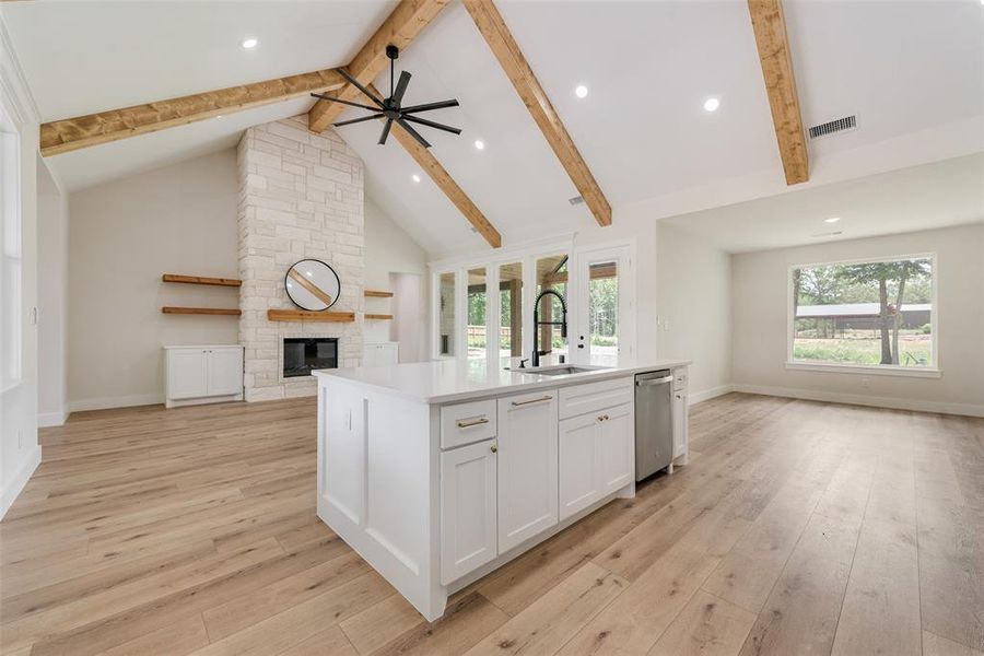 Open-concept living area featuring a vaulted ceiling with exposed wood beams, a stone-clad fireplace, and wood-finish flooring