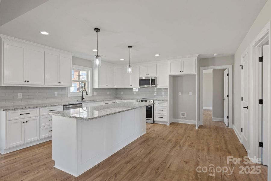 Stunning designer kitchen with white custom cabinetry, a large granite island, subway tile backsplash, and modern pendant lighting—perfect for cooking and hosting. Stunning designer kitchen with white custom cabinetry, a large granite island, subway tile backsplash, and modern pendant lighting—perfect for cooking and hosting.