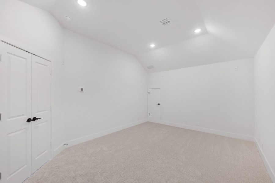 Empty bedroom with vaulted ceiling, carpet flooring, closet doors, and recessed lighting