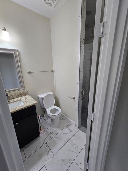 Full bath with a shower stall, marble look tile flooring, vanity, and toilet