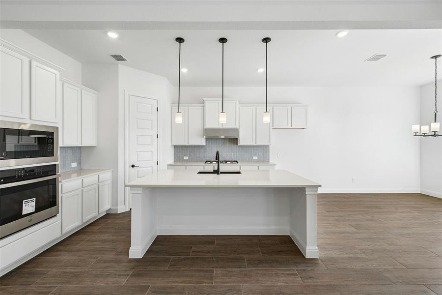 Open-concept kitchen featuring an island with a sink, white cabinetry, stainless steel built-in appliances, a tiled backsplash, and wood-finish flooring