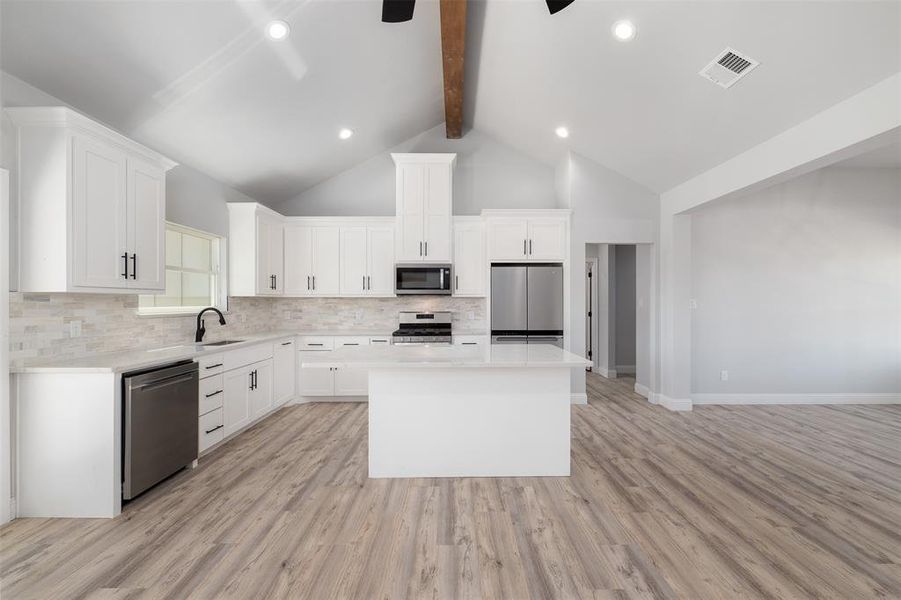 Kitchen with stainless steel appliances, beam ceiling, a sink, tasteful backsplash, and visible vents