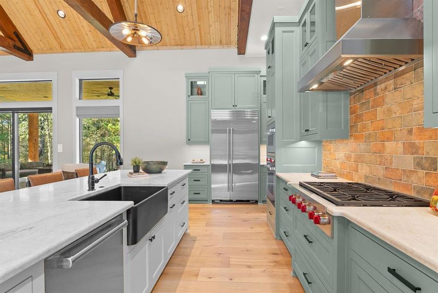 Kitchen with glass insert cabinets, backsplash, wall chimney range hood, stainless steel appliances, and light wood-style flooring