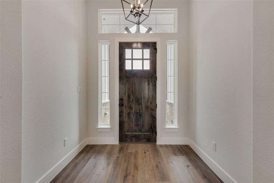 Foyer entrance with an inviting chandelier, wood-type flooring, and a healthy amount of sunlight