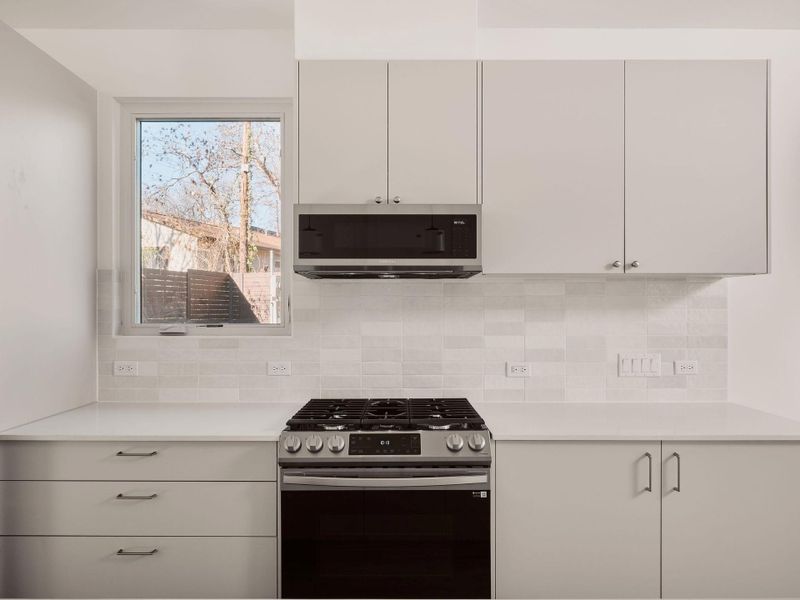 Kitchen featuring appliances with stainless steel finishes, white cabinets, light stone countertops, and tasteful backsplash