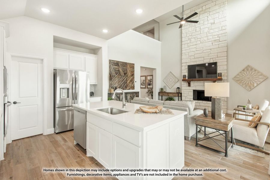 Open-concept kitchen with white island and stainless appliances flowing into living room with stone fireplace and high ceilings