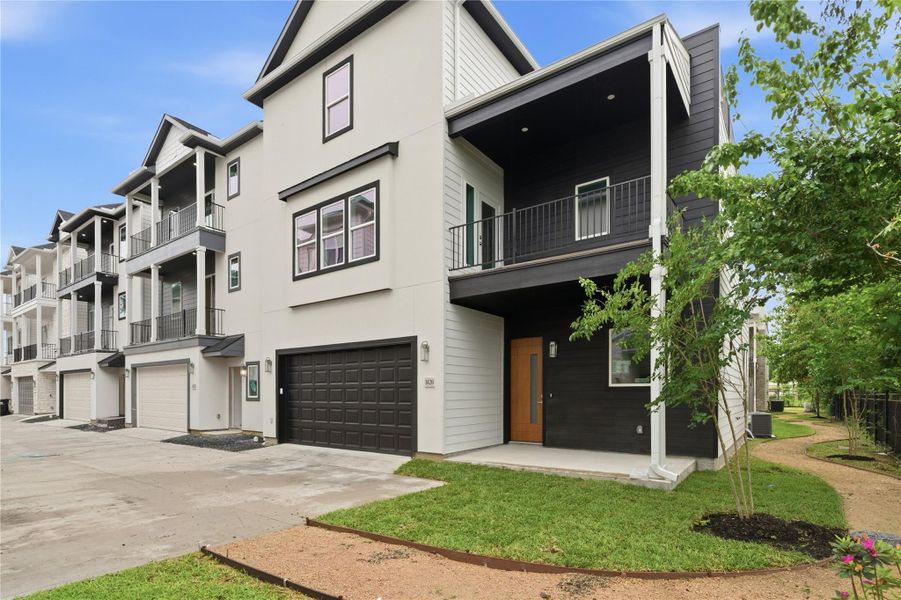 Sleek facade, featuring a two-car garage and a covered balcony. The front yard is neatly landscaped with a small garden