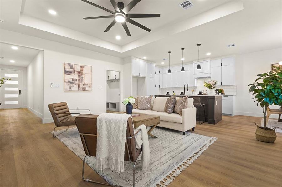 Living room with a raised ceiling, recessed lighting, light wood finished floors, and a ceiling fan