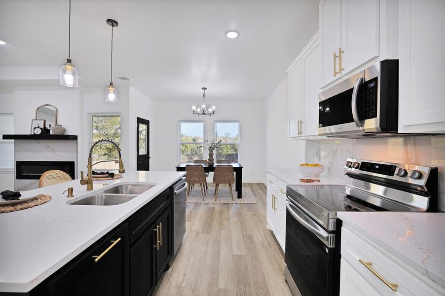 Kitchen featuring white cabinetry, sink, stainless steel appliances, a chandelier, and decorative light fixtures