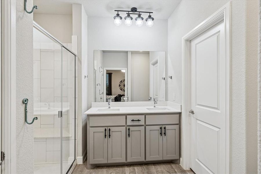 Primary bathroom featuring a shower stall, double vanity, wood finished floors, and track lighting Primary bathroom featuring a shower stall, double vanity, wood finished floors, and track lighting
