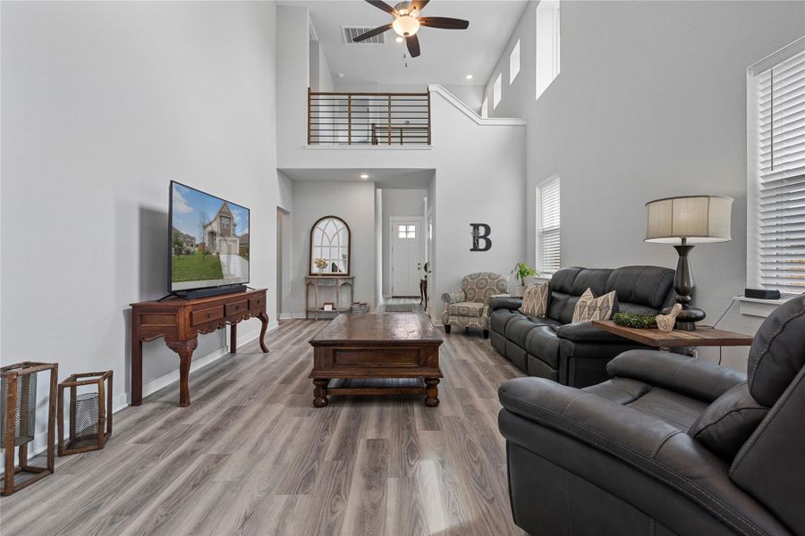 Living room featuring ceiling fan, a high ceiling, wood finished floors, recessed lighting, and baseboards Living room featuring ceiling fan, a high ceiling, wood finished floors, recessed lighting, and baseboards