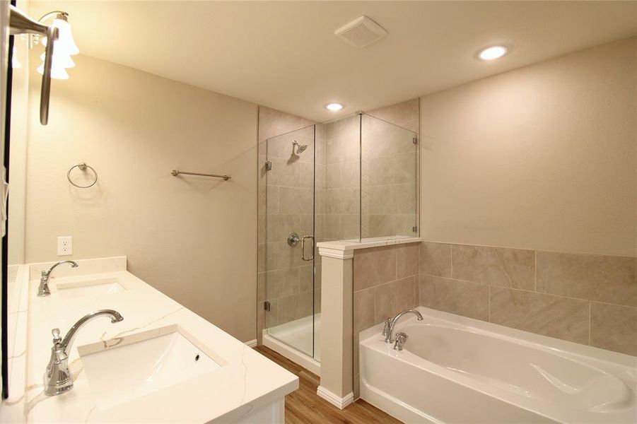 Bathroom featuring a garden tub, a stall shower, double vanity, wood finished floors, and recessed lighting