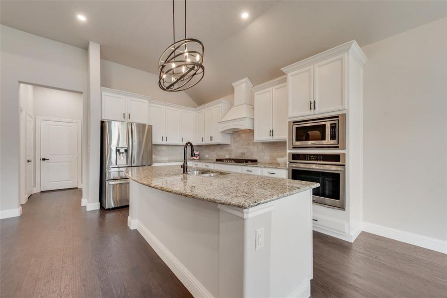 Kitchen featuring white cabinetry, backsplash, light stone countertops, stainless steel appliances, and lofted ceiling Kitchen featuring white cabinetry, backsplash, light stone countertops, stainless steel appliances, and lofted ceiling