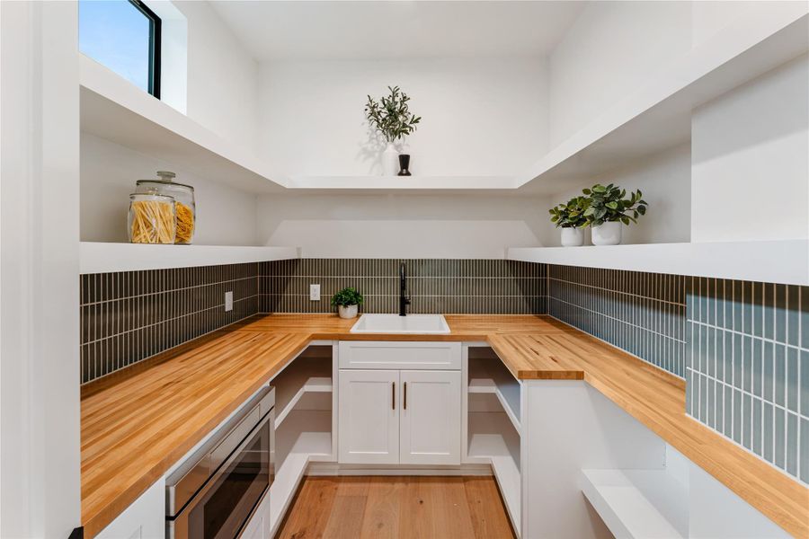 Spacious working pantry serves as a practical workspace, featuring a convenient prep sink, extensive custom shelving, and built-in microwave. This well-appointed room provides ample storage for small appliances while keeping the main kitchen beautifully uncluttered.