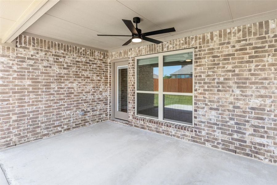 Covered back patio with ceiling fan, brick walls, concrete floor, and sliding glass door to backyard
