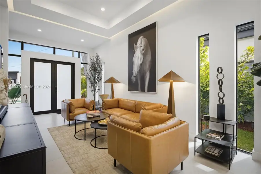 High-ceiling room featuring a recessed tray ceiling, large-format tile flooring, oversized black-framed double entry doors, and floor-to-ceiling vertical windows