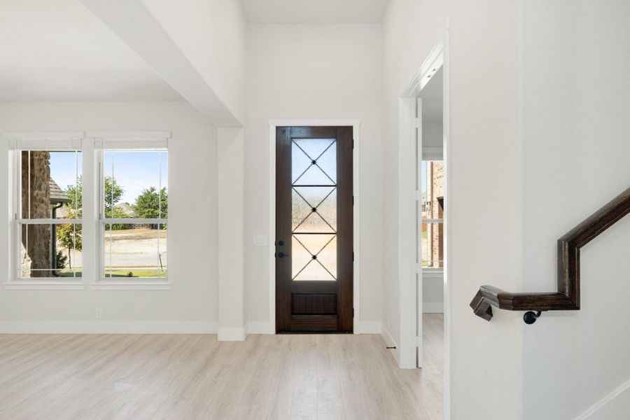 Bright home entryway with dark wood front door, glass panels, light hardwood floors, and staircase railing