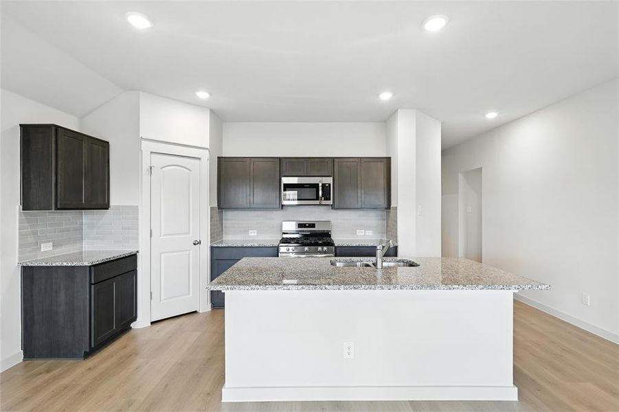 Kitchen featuring light stone counters, tasteful backsplash, appliances with stainless steel finishes, light wood-style floors, and a center island with sink Kitchen featuring light stone counters, tasteful backsplash, appliances with stainless steel finishes, light wood-style floors, and a center island with sink