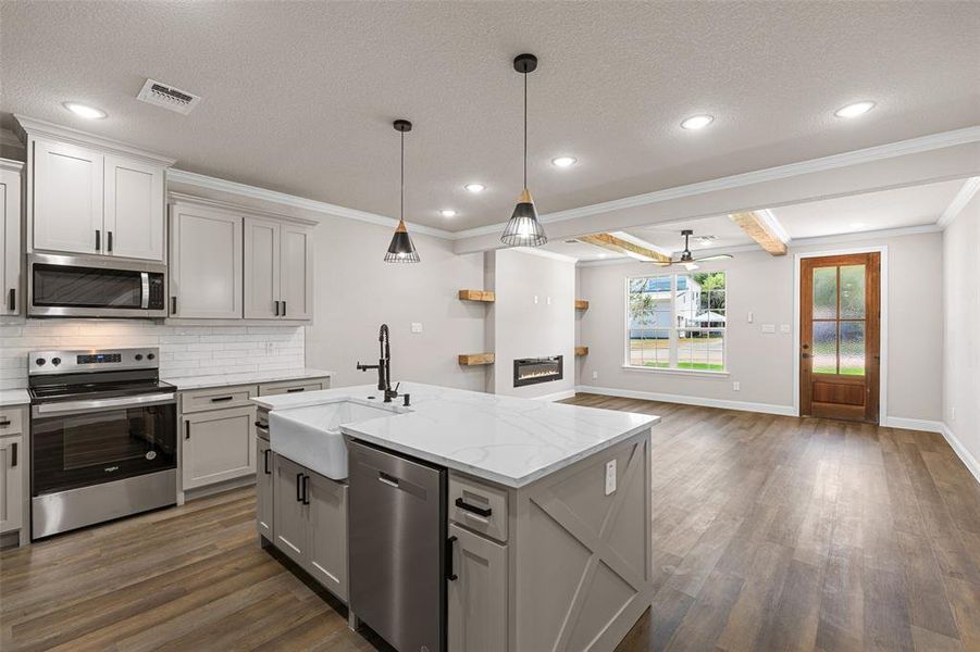 Kitchen with stainless steel appliances, sink, a center island with sink, ceiling fan, and dark wood-type flooring