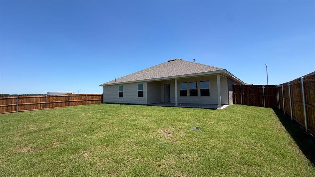Expansive rear yard featuring a privacy fence, concrete patio, and a light-colored stucco exterior with multiple windows