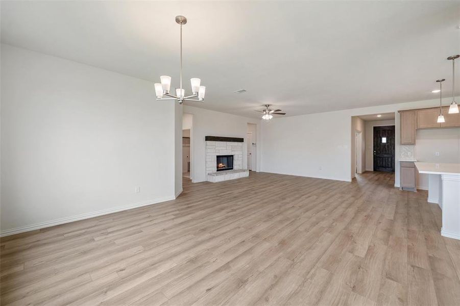 Unfurnished living room featuring a stone fireplace, light wood-type flooring, a chandelier, and ceiling fan