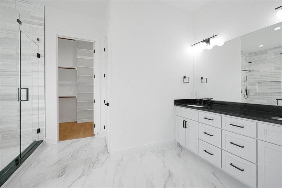 Full bath featuring a stall shower, double vanity, a spacious closet, light marble finish floors, and recessed lighting