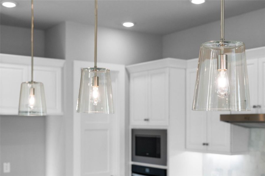 Contemporary pendant lights hang above the island, adding a touch of modern design, complemented by recessed lighting throughout the ceiling for overall illumination.