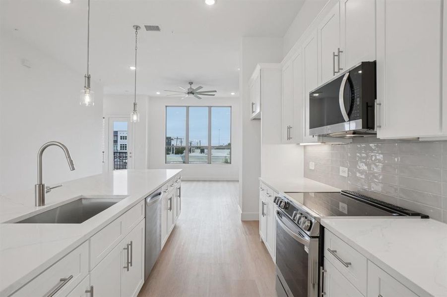 Kitchen with stainless steel appliances, white cabinetry, decorative light fixtures, light stone counters, and light wood-type flooring