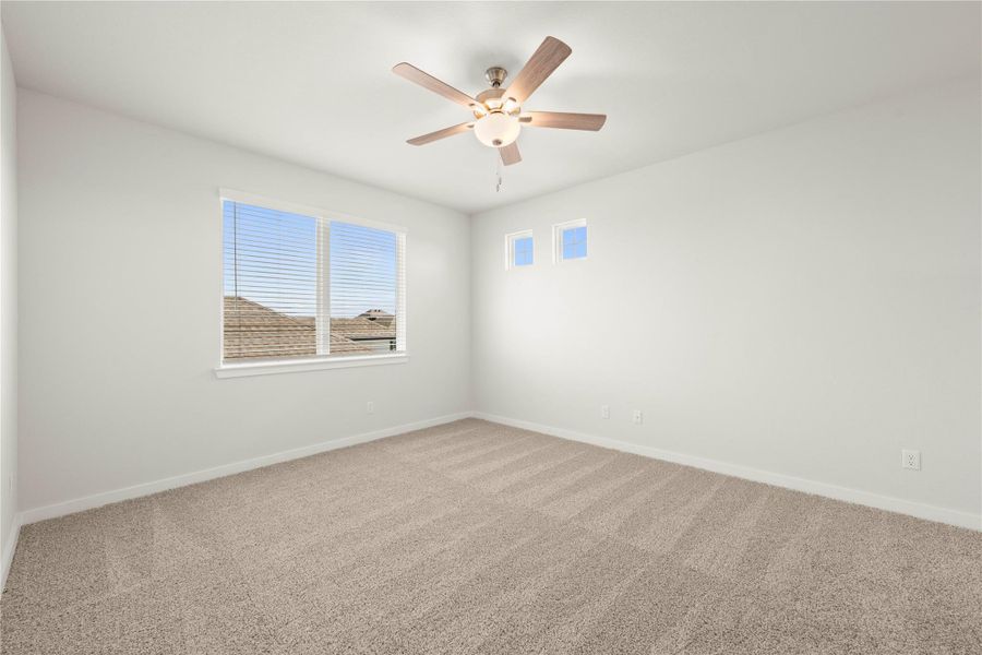 A well-lit bedroom provides ample natural illumination and comfort with plush carpeting and a modern ceiling fan.