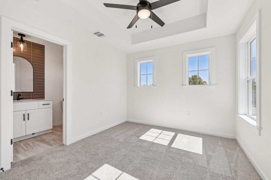 Unfurnished bedroom featuring a raised ceiling, light colored carpet, a ceiling fan, and ensuite bathroom Unfurnished bedroom featuring a raised ceiling, light colored carpet, a ceiling fan, and ensuite bathroom