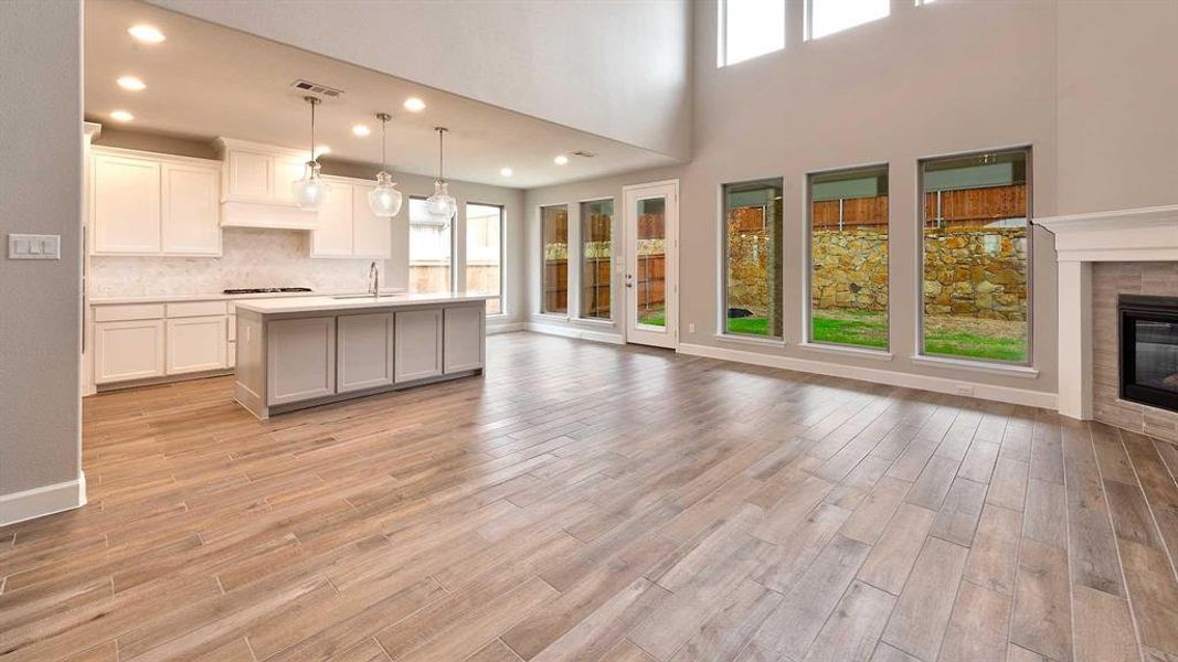 Kitchen featuring gas stovetop, decorative light fixtures, a center island with sink, a tiled fireplace, and white cabinets