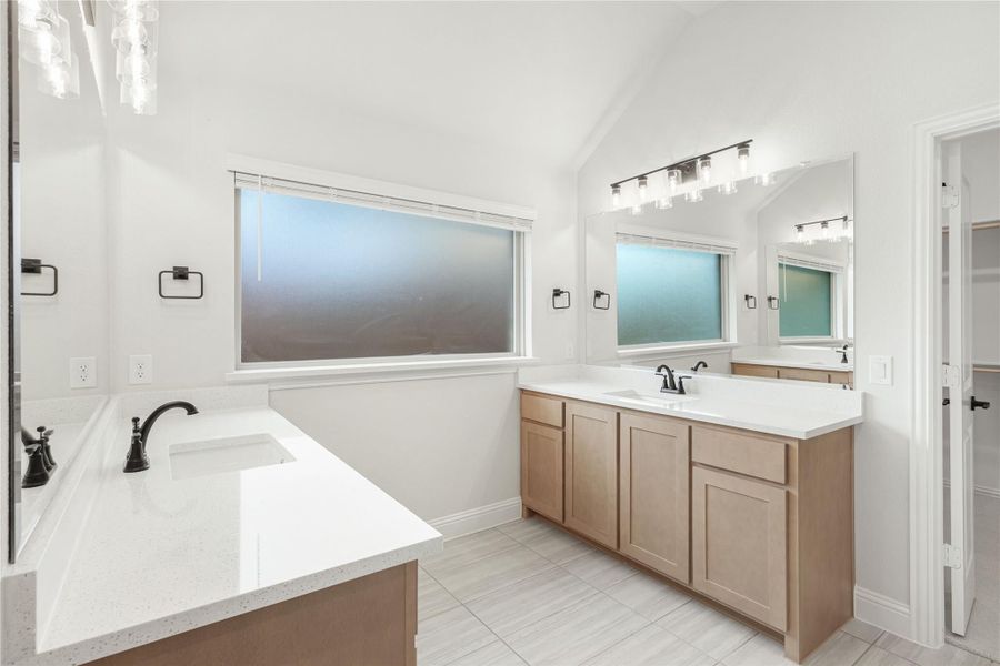 Dual-sink master bathroom with light wood cabinets, white quartz countertops, and vaulted ceiling