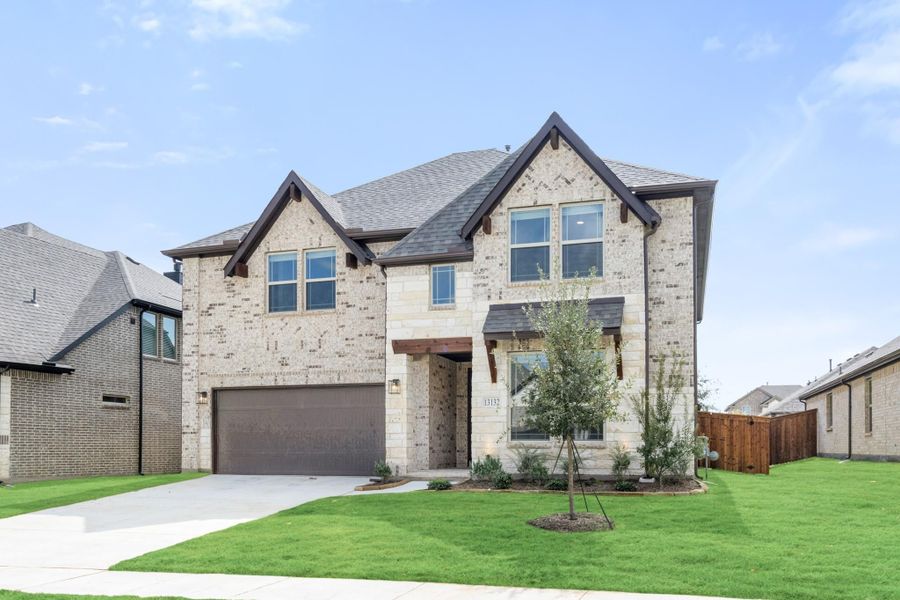 Two-story home with light brick exterior, two-car garage, and green front lawn