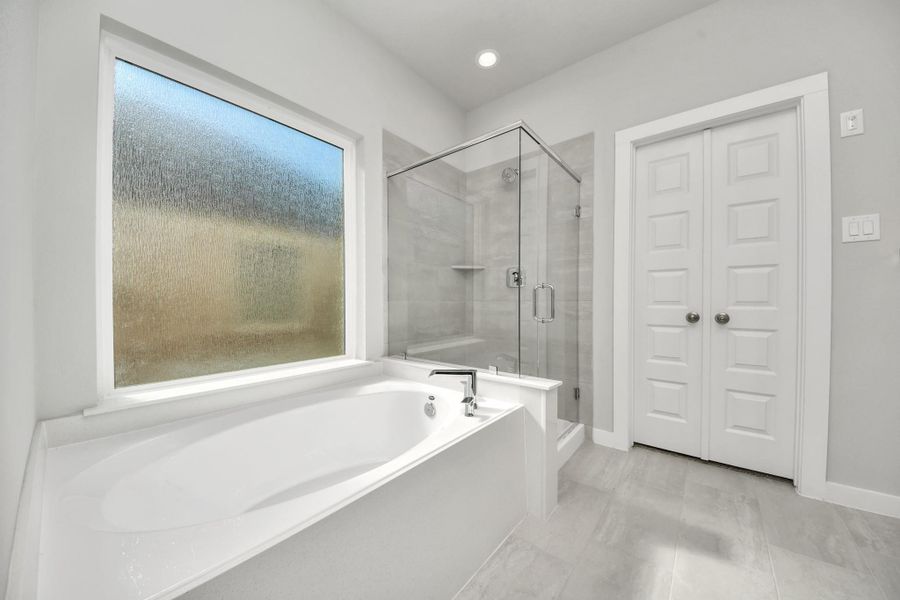 Indulge in a spa-like retreat within the confines of this primary bathroom. Delight in a spacious walk-in shower enveloped in stylish tile surround, unwind in a separate garden tub adorned with custom detailing. Sample photo of completed home with similar floor plan. Actual colors and selections may vary.